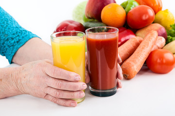 Women hands of an elderly woman holding two glasses of orange juice and tomato next to vegetables