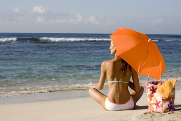 femme en maillot de bain assise sous une ombrelle sur la plage au bord de la mer