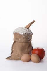 Flour in bowl with eggs and rolling pin over white background