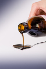 
Bottle pouring a liquid on a spoon. Isolated on a white background. Pharmacy and healthy background. Medicine. Cough and cold drug.  - 107243751