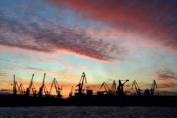 Obraz premium Silhouette of port cranes on sunset sky background