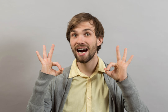 Everything is OK! Happy young man in shirt gesturing OK sign and smiling while standing against grey background