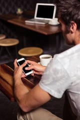 Hipster man using smartphone while drinking coffee