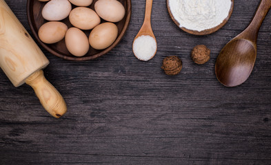 Wooden background with baking ingredients (eggs, flour and rolling pin) over rustic texture. Top view. Space for text. Food or cooking concept.