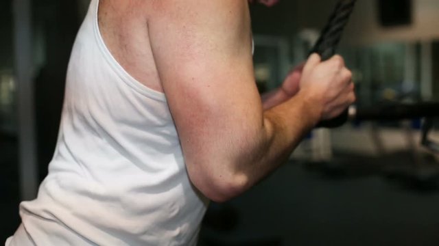 Strong young man bodybuilder pumping triceps in a gym