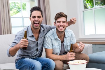 Young male friends enjoying beer while sitting on sofa