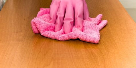 Hand in pink protective glove cleaning wooden furniture with rag. Early spring cleaning or regular clean up. Maid cleans house.