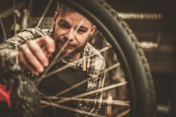 Stylish bicycle mechanic doing his professional work in workshop