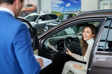 Plakat Beautiful young woman buys a car in the dealership saloon.