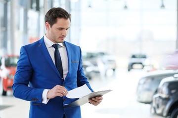 Confident young car dealer standing in showroom.