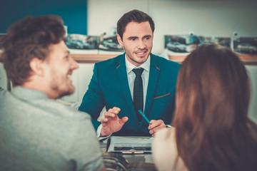 Salesman talking to a young couple at the dealership showroom.