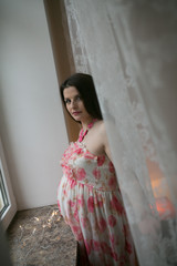 young pregnant woman staying near the window in pink dress