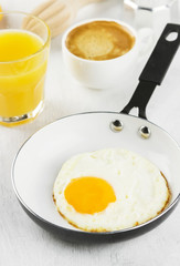 Breakfast: fried eggs in pan, orange juice, coffee on a white ba