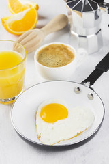 Breakfast: fried eggs in pan, orange juice, coffee on a white ba