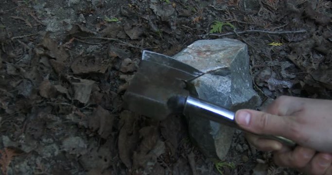 Detail of woman's hands sharpening axe on stone during camping
