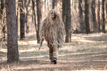 Soldier in camouflaged sniper suit  walking with gun/Soldier in camouflaged sniper suit  walking with gun in forest.Selective focus.