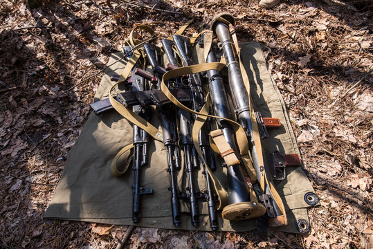 Guns on the ground/Many automatic rifles and grenade launchers lie on green piece of cloth in the forest