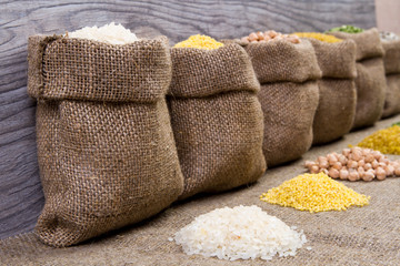Fototapeta na wymiar Set groats, peas, rice, millet, peas in sacks, burlap on wooden background