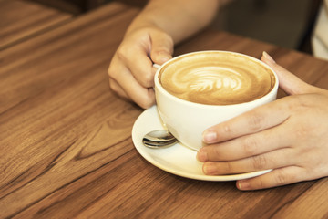 Hand holding coffee cup on wood table.