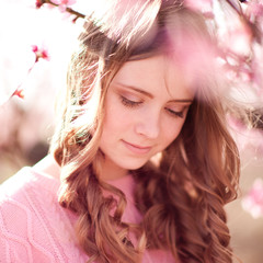 Fototapeta premium Beautiful teen girl 14-16 year old with curly hairstyle posing in peach flowers outdoors. Smiling child. 
