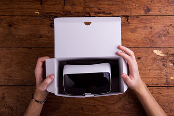 Unrecognizable man unpacking virtual reality goggles, wooden tab