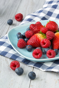 Assorted fresh berries on a plate, wooden background