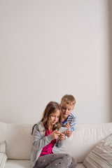 Children at home sitting on sofa, playing with smartphone