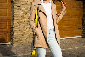 Slim girl in a beige coat, blue jeans and white shirt outdoors