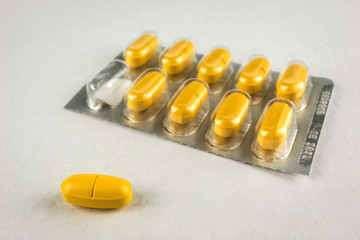 one yellow pill closeup on a background of the packaging of tabl