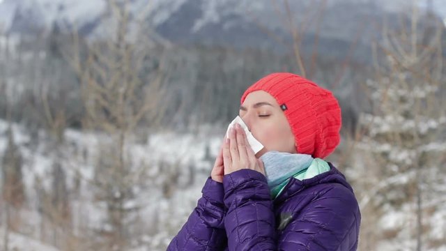 Young woman sneezes in winter mountains