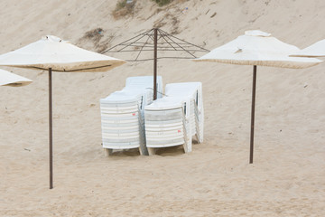 Two stacks of folded chairs on the beach with umbrellas