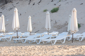 Rows of empty chairs on the beach with a deflated parasols