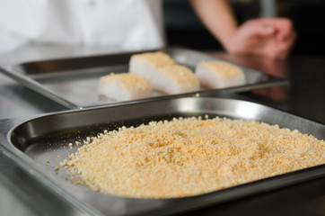 Fresh fish fillet cube covered in breadcrumbs, being placed onto a metal baking tray.