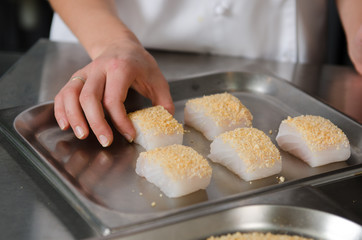 Fresh fish fillet cube covered in breadcrumbs, being placed onto a metal baking tray.