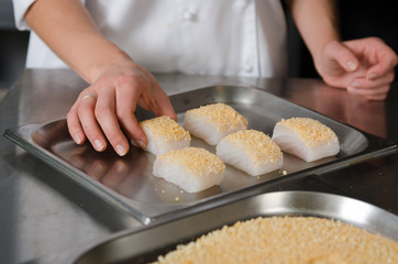 Fresh fish fillet cube covered in breadcrumbs, being placed onto a metal baking tray.