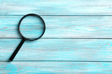 Magnifying glass on a blue wooden table - obrazy, fototapety, plakaty