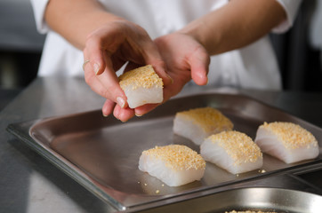 Fresh fish fillet cube covered in breadcrumbs, being placed onto a metal baking tray.