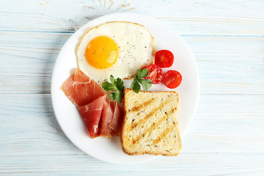Fried eggs with bacon and toasts on plate on blue wooden table