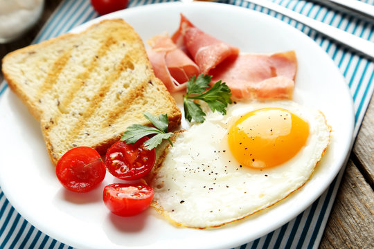 Fried eggs with bacon and toasts on plate on grey wooden table