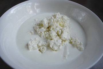 Fresh cottage cheese and milk / yogurt are in a white dish. Ingredients for dough for cheesecakes. Preparation for cooking. 