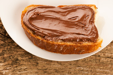Slice of bread with sweet chocolate nougat spread on white plate