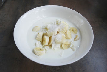 Fresh cottage cheese, banana slices, sugar and milk / yogurt are in a white dish. Ingredients for dough for cheesecakes. Preparation for cooking. 