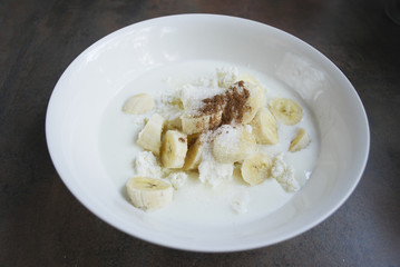 Fresh cottage cheese, banana slices, sugar, cinnamon and milk / yogurt are in a white dish. Ingredients for dough for cheesecakes. Preparation for cooking. 