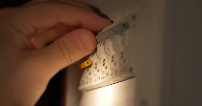 Man is switching on the fuses on the fusebox, after a power failure, in darkness using the flashligh to see.