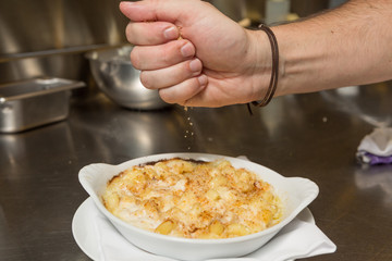 Cooked breadcrumbs being sprinkled onto oven bake macaroni cheese.