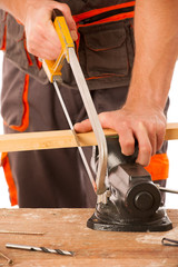Young carpenter cuts a wooden lath with a saw isolated over whit