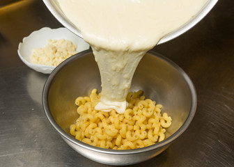 Melted cheese being poured onto cooked Macaroni pasta.