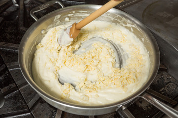 Cheese being mixed into a hot pan, to melt in preparation for Macaroni cheese