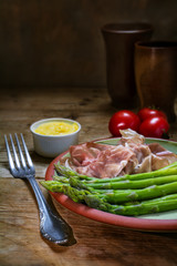 green asparagus with ham and hollandaise sauce on an plate, rustic wooden table, vertical