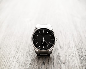 Silver reflective wrist watch with black dial on wood surface